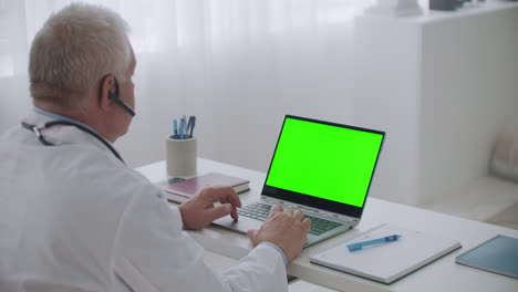 Erfahrener-Arzt-Hört-Patienten-Oder-Kollegen-Per-Videoanruf-Auf-Laptop-Mit-Grünem-Display-Für-Chroma-Key-Technologie-Zu